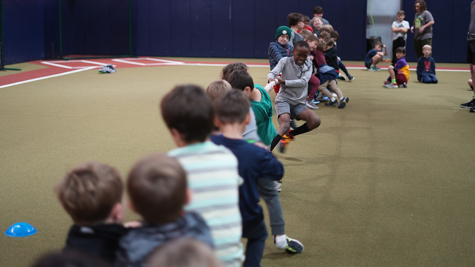 Two teams of campers pulling in a wide tug-o-war across the indoor turf at JPLEX